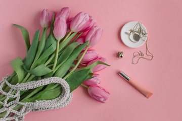 Bunch of spring flowers in string bag, female accessories on pink background. Woman Day, Valentine's Day concept.