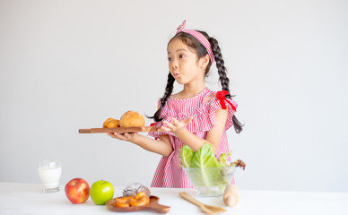 Portrait of little girl show action of surprise and hold plate with bread in front of white wall background.