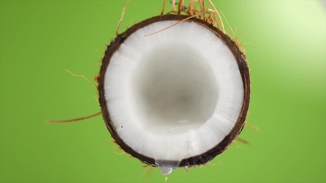 Coconut pouring water, dripping coconut milk, drops of coco nuts oil over green background. Tropical Coco nut closeup. Healthy Food, skin care concept. Vegan food. 4K UHD video, slow motion