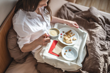 Young woman have a romantic Breakfast in morning bed. Coffee and word love from cookies. Surprise on Valentine's day