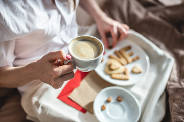 Young woman have a romantic Breakfast in morning bed. Coffee and word love from cookies. Surprise on Valentine's day