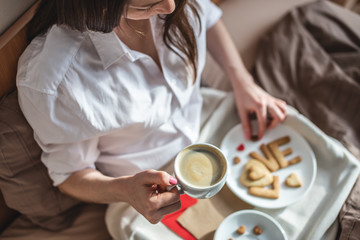 Young woman have a romantic Breakfast in morning bed. Coffee and word love from cookies. Surprise on Valentine's day
