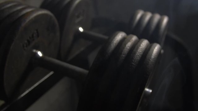 Close Up Pan Along Of Weights Lined Up On Weight Rack In Industrial Gym Old Style Old Fashioned Under Ground Gym. Paint Work Scratched Off Smoke Passing Over