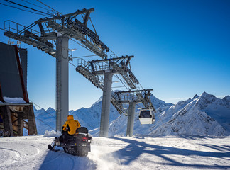 Snowmobile with a driver in motion. Cableway in movement on rise and descent on background...