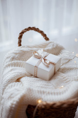 small white gift box with ribbon on a knitted sweater, wicker basket, Christmas lights.
