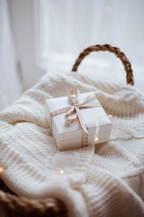 small white gift box with ribbon on a knitted sweater, wicker basket, Christmas lights.