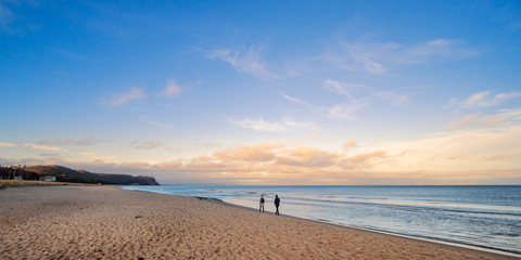 Leute gehen am Meer spazieren, mit Wolken am Horizont und blauem Himmel