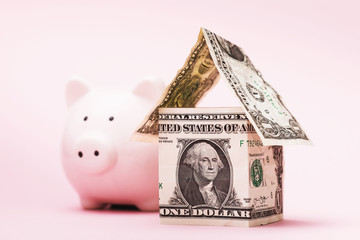 House of dollars and piggy bank on a pink background. The concept of accumulating money for housing