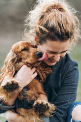 Portrait of cute cocker spaniel on hands of attractive happy smiling young curly woman. Love...