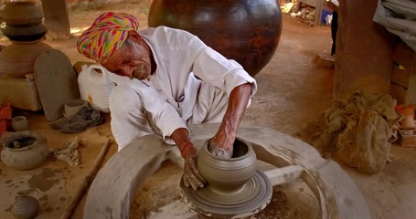 Skilled professional potter throwing the potter's wheel and shaping traditional ceramic vessel and clay ware: pot, jar in pottery workshop. Handwork craft from Shilpagram, Udaipur, Rajasthan, India