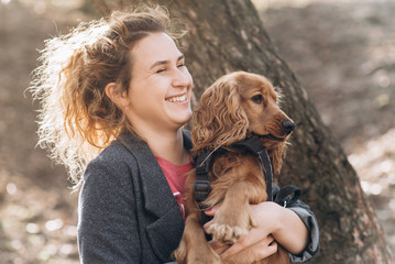 Attractive young curly woman smiling and holding her cute brown dog