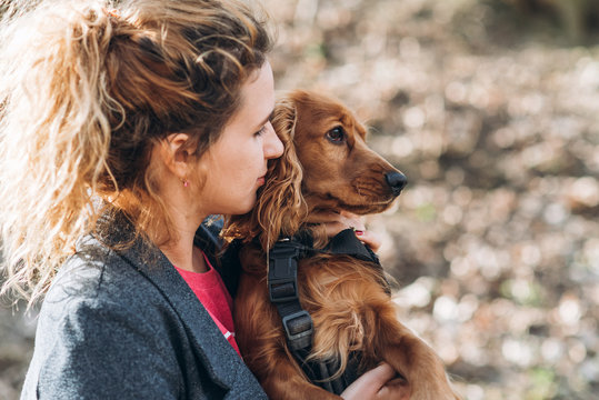 Attractive curly young woman hugs her brown dog outdoor