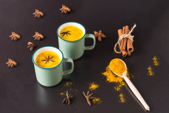 Golden turmeric latte milk tea with curcuma powder in mugs on black background.