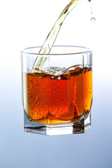 Whiskey pouring from the neck of a bottle into a glass on a wooden stand