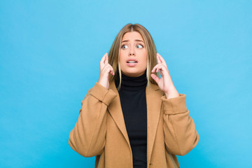 young blonde woman crossing fingers anxiously and hoping for good luck with a worried look against...