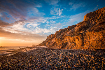 Beautiful beach sunset with sunlit bluffs and a rocky shore - obrazy, fototapety, plakaty