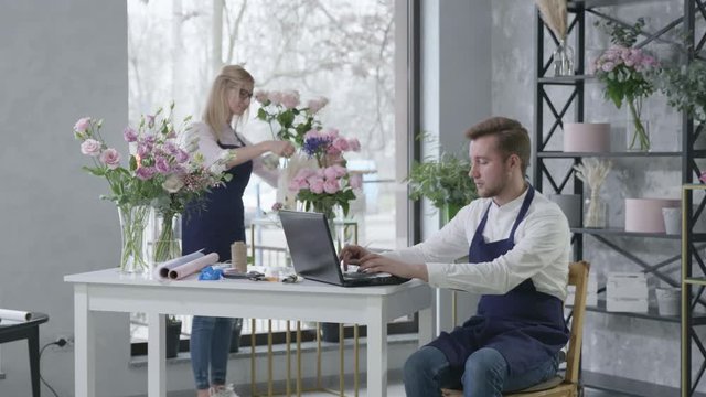 florists a man and his female employee looking at display of a portable computer and accepting orders from clients for flower delivery, modern floristic salon provides flower delivery
