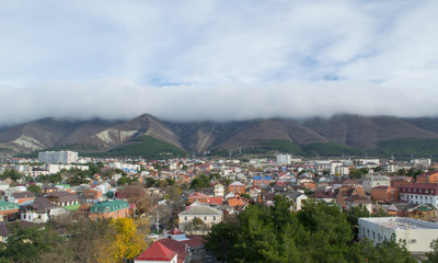 Fototapeta premium City and behind mountains with peaks in the clouds. Summer