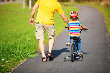 a child on a bicycle in helmet with father on asphalt road