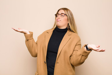 young blonde woman shrugging with a dumb, crazy, confused, puzzled expression, feeling annoyed and...