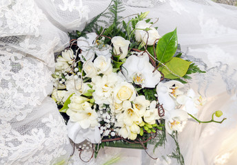 Ramo con rosas, lirios y orquídeas blancas y hojas verdes sobre el vestido de una novia