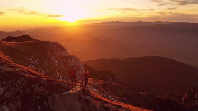 Aerial 4k drone clip with couple of hikers watching a beautiful sunset on top of Bucegi mountain ridge, during magical golden hour light in autumn season, in Romania