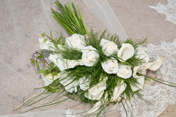 Ramo  de rosas y calas de color blanco sobre el velo de una novia en el suelo