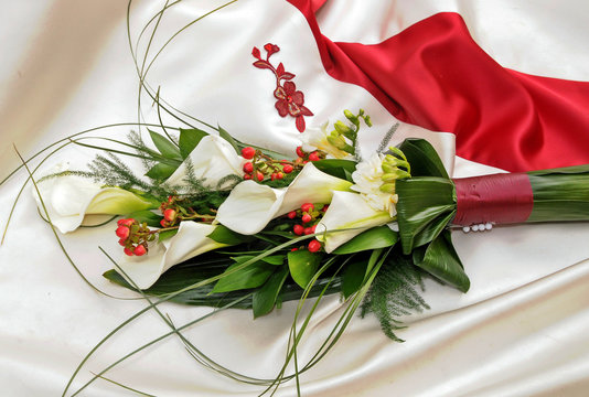 Ramo de flores de alcatraz blanco sobre vestido de novia con adornos rojos