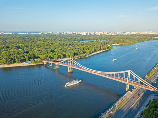 Fototapeta na wymiar Aeiral drone view. The boat floats under a pedestrian bridge along the Dnieper River in Kiev.