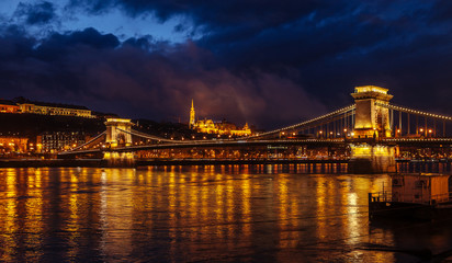 Fototapeta na wymiar Night View Of Szechenyi Bridge. Famous Chain Bridge Of Budapest. Beautiful lighting and reflection in the Danube River.