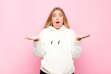 young blonde woman feeling extremely shocked and surprised, anxious and panicking, with a stressed...
