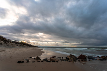 Fototapeta na wymiar Baltic sea beach with stones and old breakwaters under a gloomy cloudy sky at long exposure at dusk