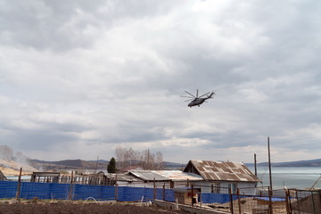A helicopter flies over a forest fire over a rural village house in early spring.