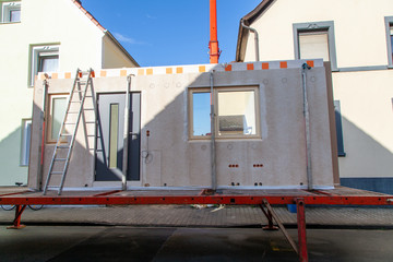 Truck trailer in orange with component for a prefabricated house of a ladder leaning against it and...