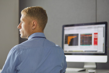 Young businessman working in office, sitting at desk, looking at laptop computer screen, smiling