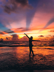 Silhouette of a thin girl in a hat on the seacoast on the background of  wonderful sunset. The sun's rays break through the clouds. Sense of freedom. Mesmerizing landscape. The vertical position 