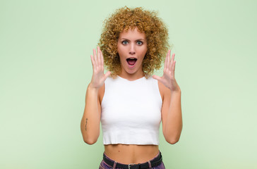 young afro woman looking shocked and astonished, with jaw dropped in surprise when realizing...
