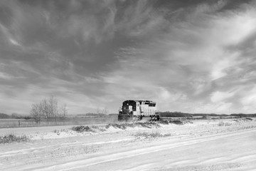 A red locomotive engine travelling down a railway track in a forested black and white prairie winter landscape