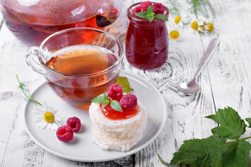 Raspberry jam on pieces of white wheat bread and freshly brewed tea on white wooden table