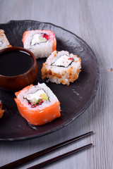 Sushi rolls assortment and soy sauce served on round plate on grey wooden table
