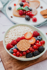 Oatmeal with berries in bowl for breakfast on blue background. Healthy food concept.