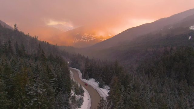 AERIAL: Tourists on a fun road trip drive along the scenic mountain road in British Columbia, Canada. Flying behind a car cruising down the famous touristy Sea to Sky Highway at gorgeous sunset.