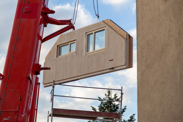 Truck crane has component from prefabricated house to construction site with visible scaffolding