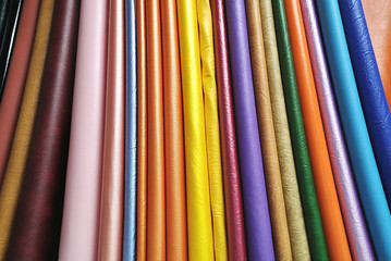 Multicolored rolls of artificial leather for sale in a fabric store. Vertical textile samples.
