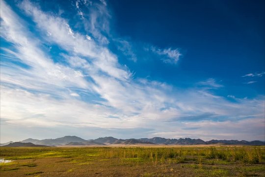 time lapse of white fluffy clouds in blue sky over plain at root of mountains 