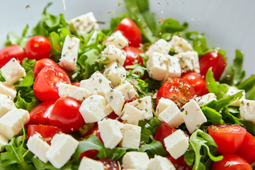 Vegetable salad dish, closeup. Red cherry tomatoes with salad cheese, fresh green arugula and condiments