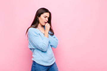 young pretty woman feeling ill with a sore throat and flu symptoms, coughing with mouth covered...