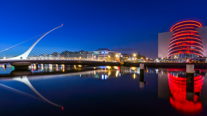 Naklejka premium Blue hour at Dublin docks, Samuel Beckett bridge and convention centre. Illuminated embankment and blurred water. long exposure photography, Ireland