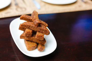 Pile of appetizing toasted rye bread sticks. Toasts made of season bread. White plate. dark background. Close-up, top view