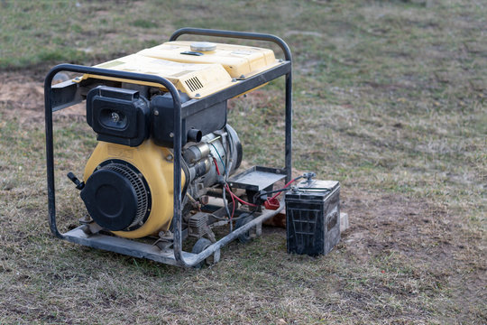 close-up. Street lighting. A gasoline-powered generator that produces current. A car battery is connected for charging. Backup or emergency power source. The generator is not new